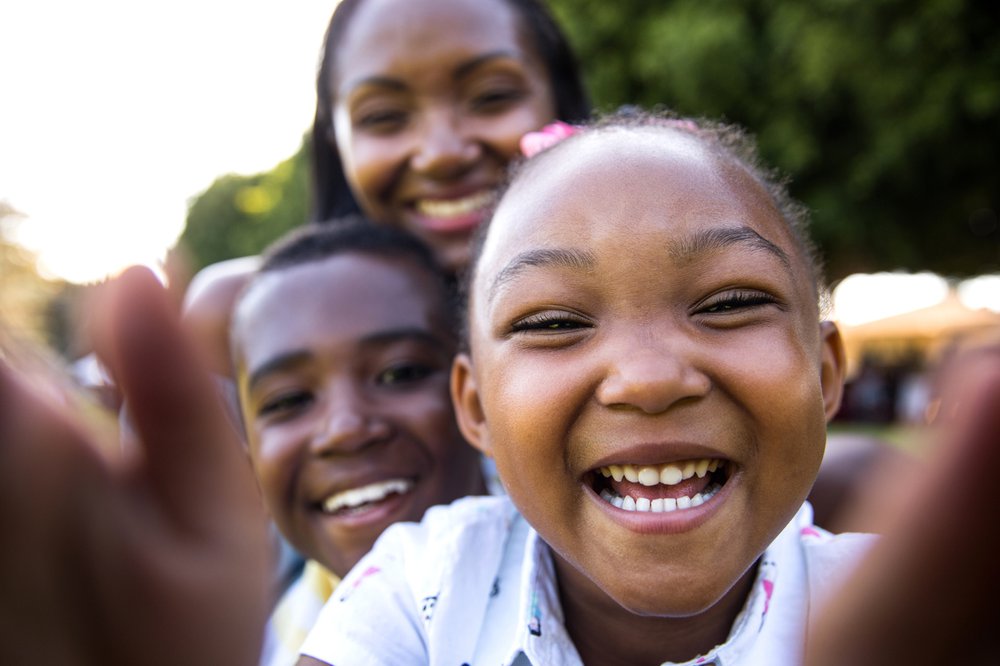 Two laughing children taking a selfie with their mother smiling in the background