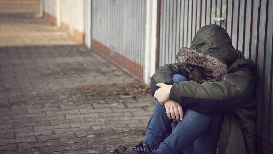 Worried looking child sitting on the floor against metal fence