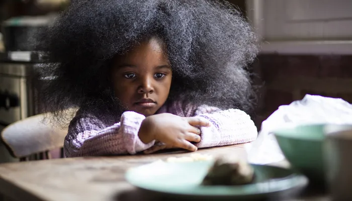 Worried young girl sits at table with empty plate