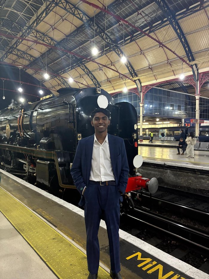 Young Ambassador, Yashneil, standing in front of a steam train and smiling at the camera