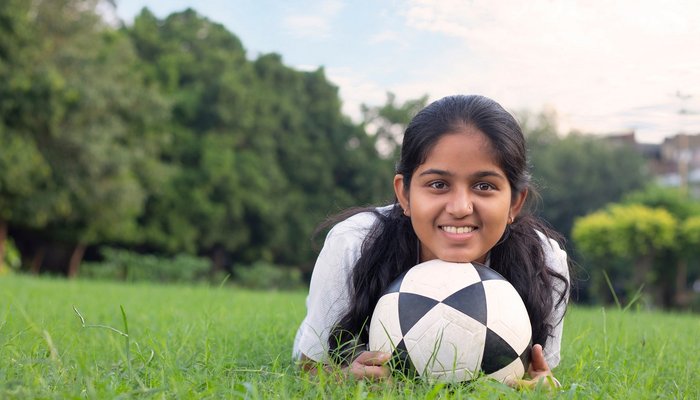 Young girl laying on the grass with a football, smiling into the camera
