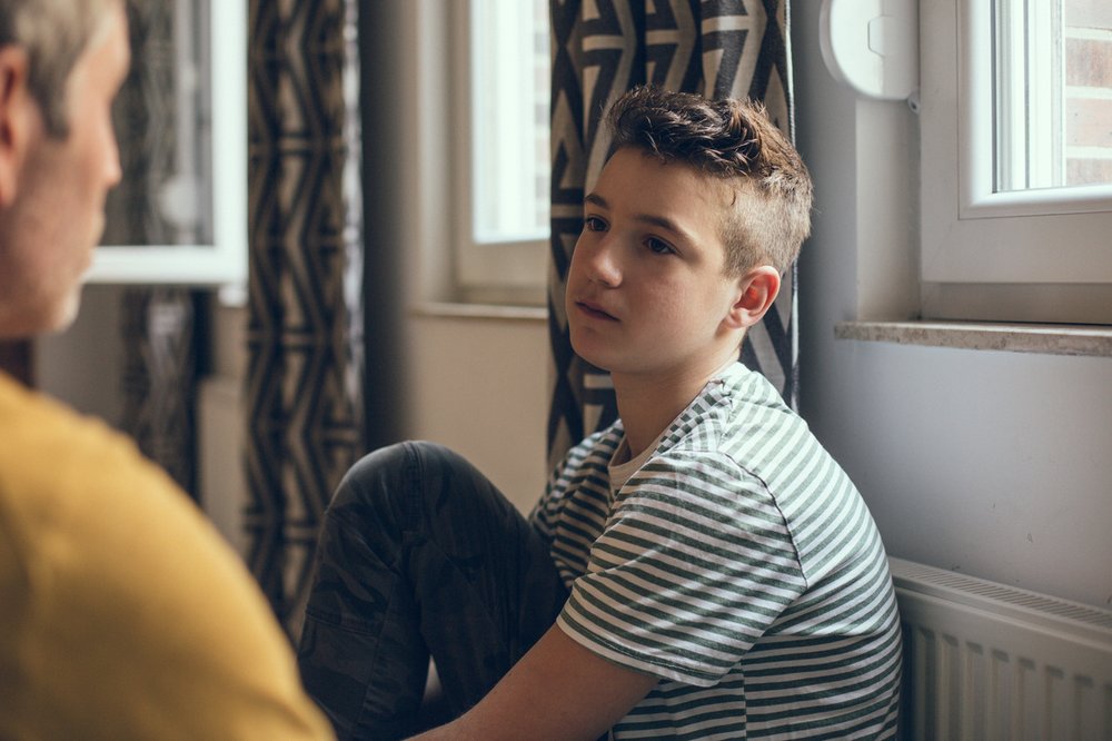 Young boy seated looking at his father with a straight face