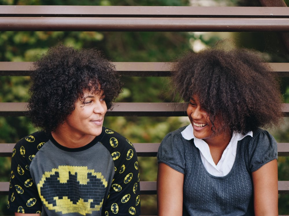 Two happy teenage girls sitting on a bench and smiling at each other