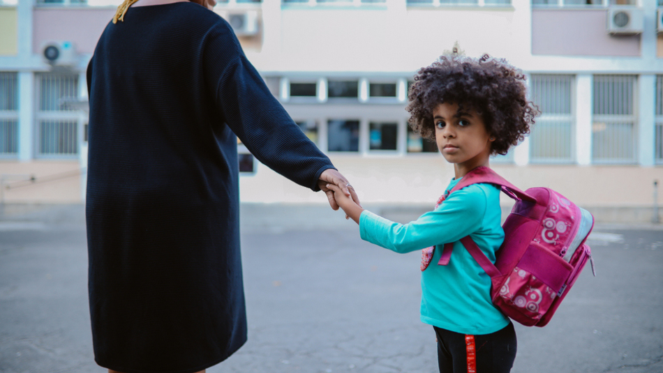 Young girl holding her mum's hand looks back at camera with a straight face