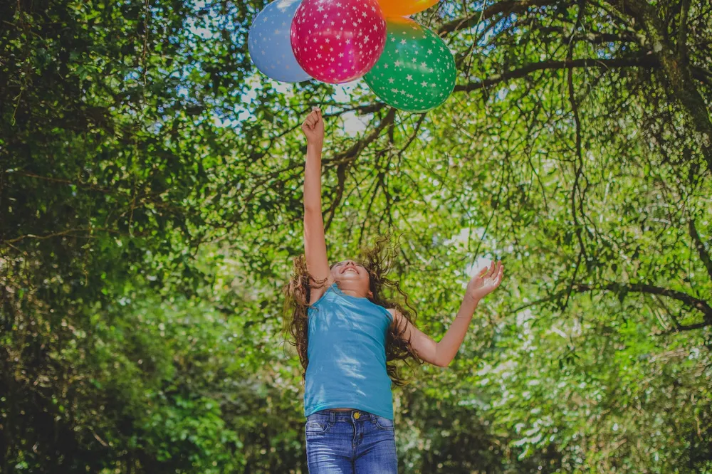 Young happy girl jumping in the air to catch balloons in park