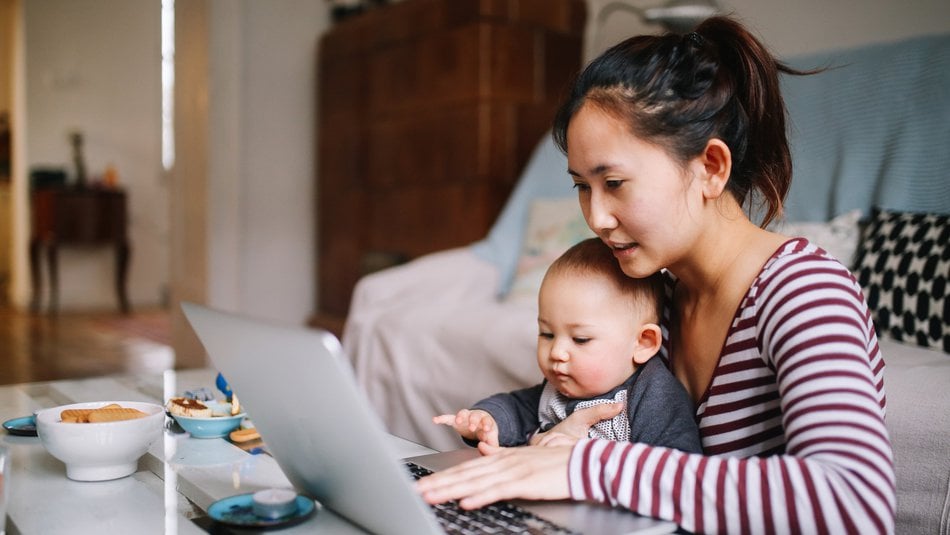 Young mother working on laptop with son in her lap