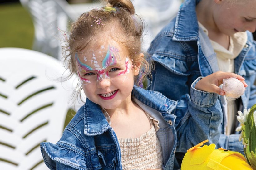 Young girl smiling at the camera, her face is painted as a unicorn.