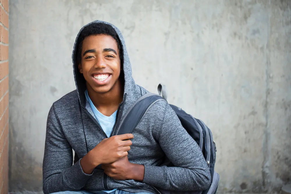 Young teenage boy with big smile wearing backpack and hoodie.jpg