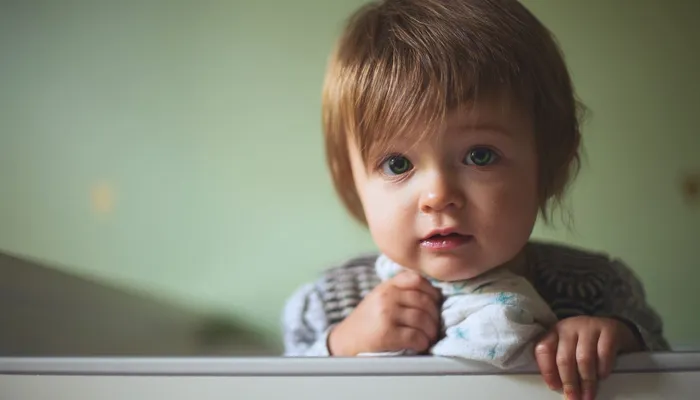Young toddler leaning against cot with snuggly blanket