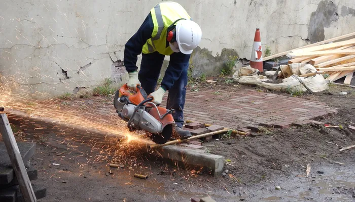 Young person sending sparks flying while using an angle grinder to cut a metal pole