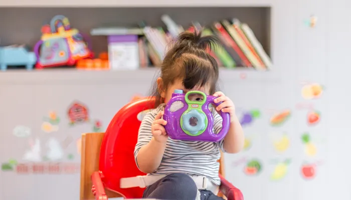 Toddler sitting in high chair and playing with toy camera