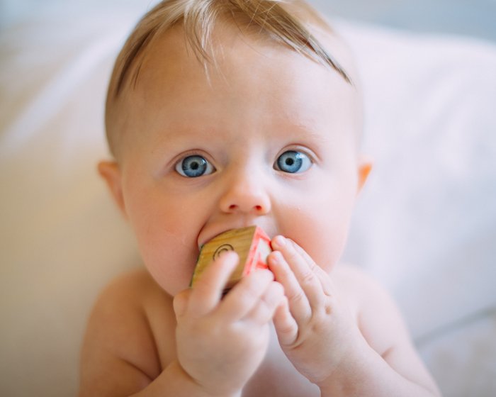 Young baby with bright blue eyes playing with a wooden block