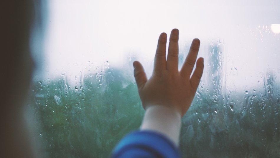 child's hand on rainy window