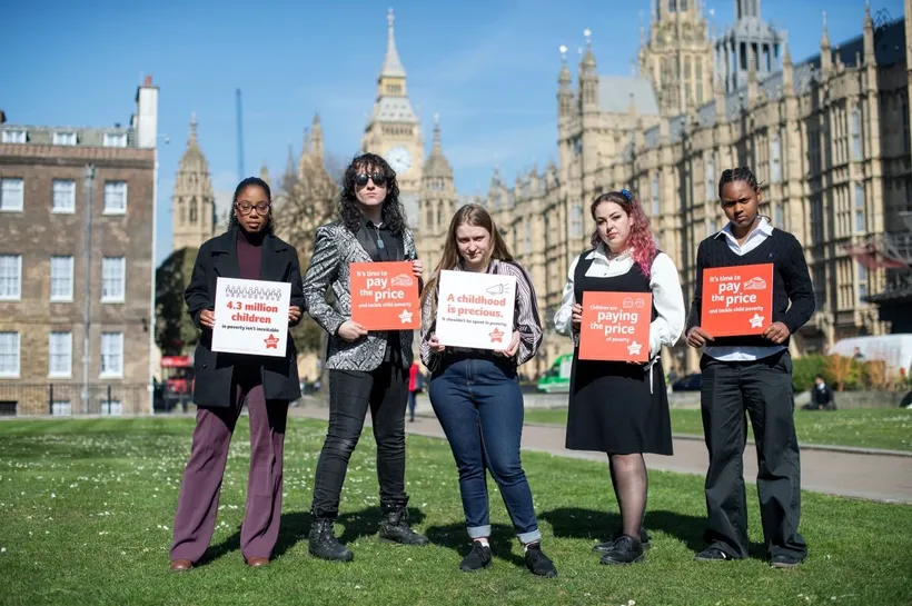 five young campaigners outside parliament holding Paying the Price campaign placquards