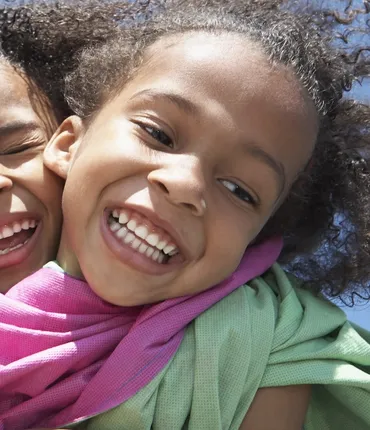 Happy girl hugging her friend from behind with bright blue sky in background