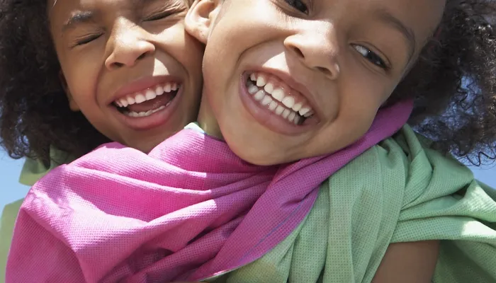 Happy girl hugging her friend from behind with bright blue sky in background