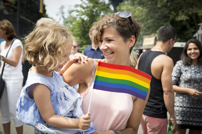 A young mother with her daughter in her arms waving a rainbow flag