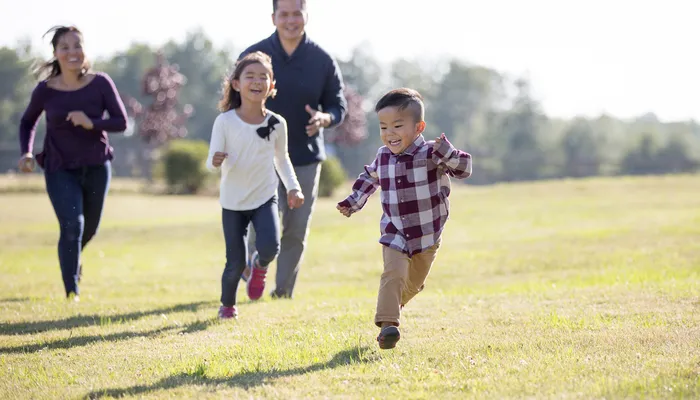 Two happy young children running in a field with their parents running close behind