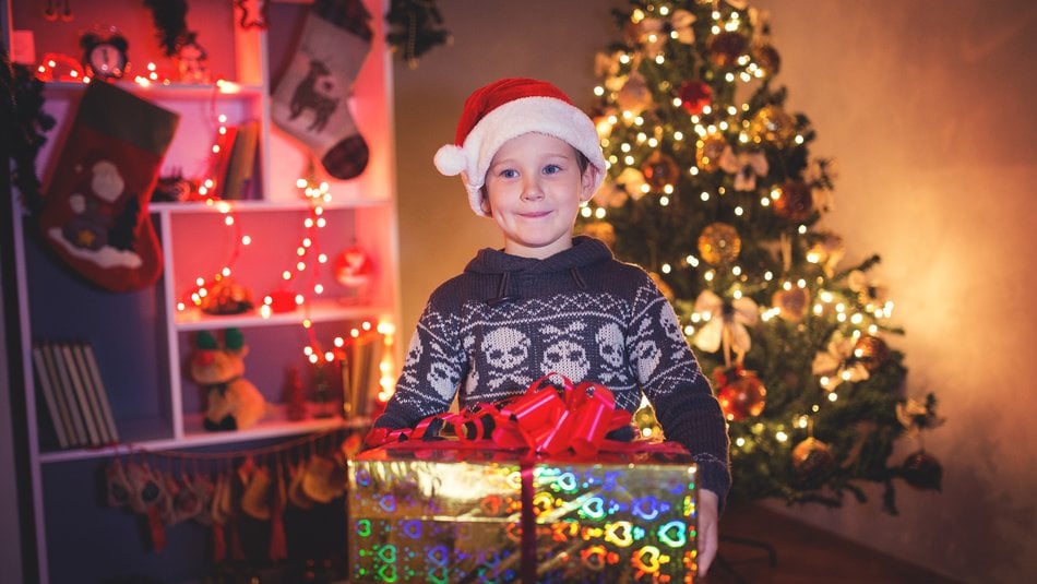 Boy carrying Christmas present in front of Christmas tree