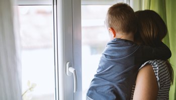 Mother and son looking through window at home