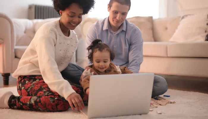 Young couple with baby girl sitting on floor in front of laptop
