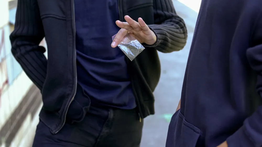A boy handing over a bag of drugs to someone