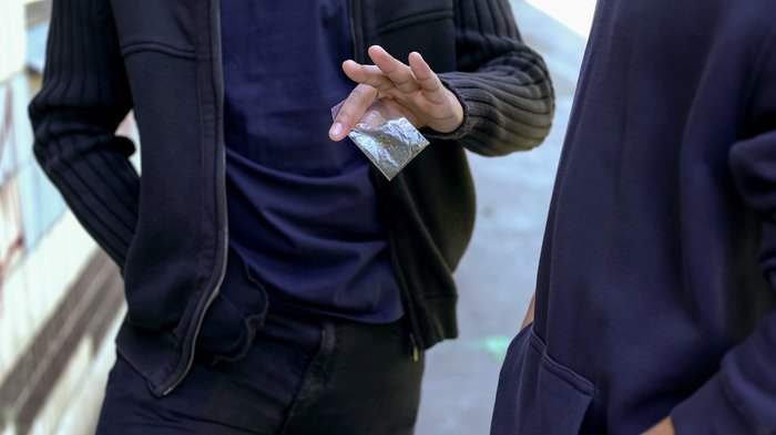 A boy handing over a bag of drugs to someone