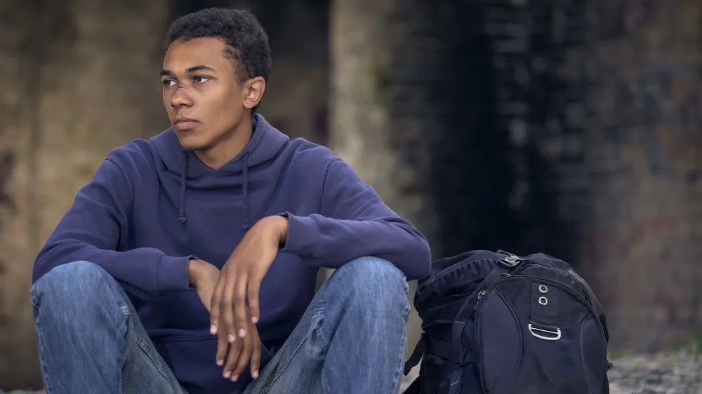 Boy sitting on ground with rucksack - boy has a cut to his face