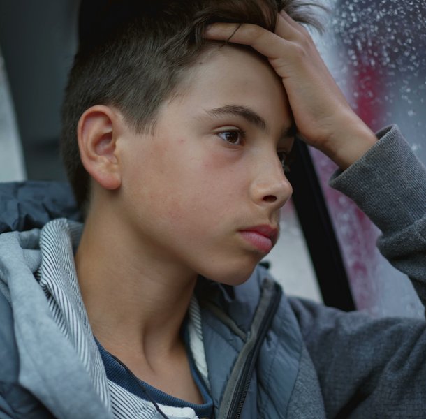 Boy looking out window thinking whilst its raining outside