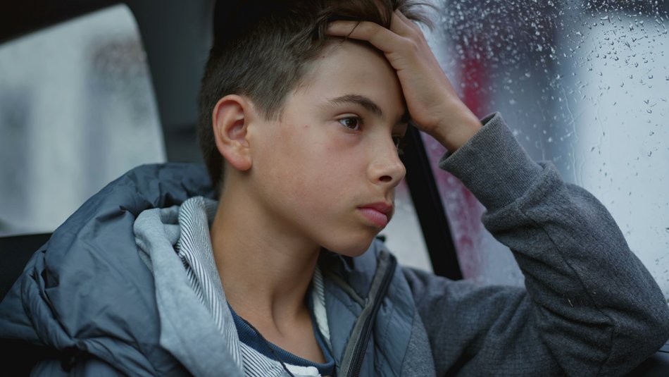 Boy looking out window thinking whilst its raining outside