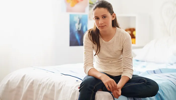 teenage girl sitting on her bed at home looking blankly into camera