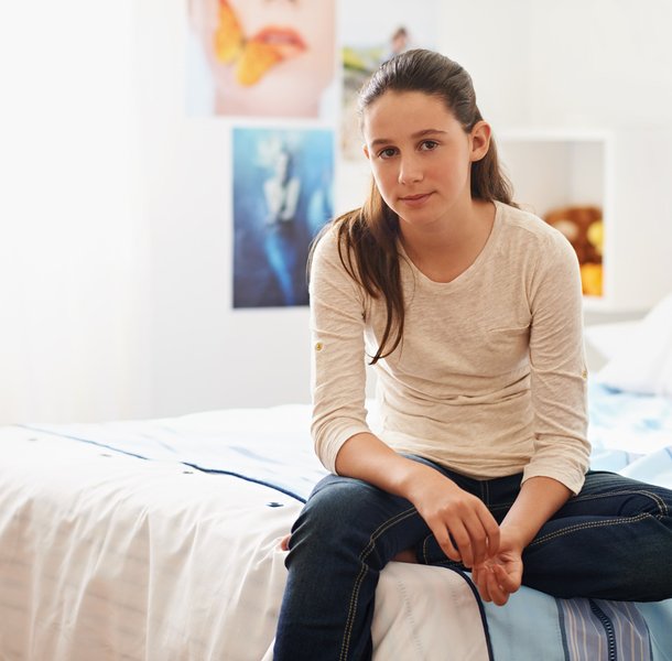 teenage girl sitting on her bed at home looking blankly into camera
