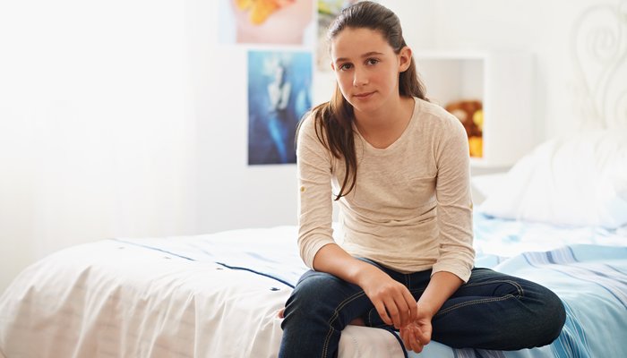 teenage girl sitting on her bed at home looking blankly into camera
