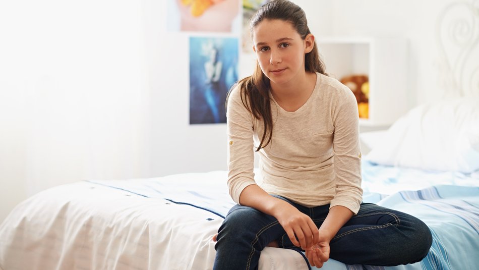 teenage girl sitting on her bed at home looking blankly into camera