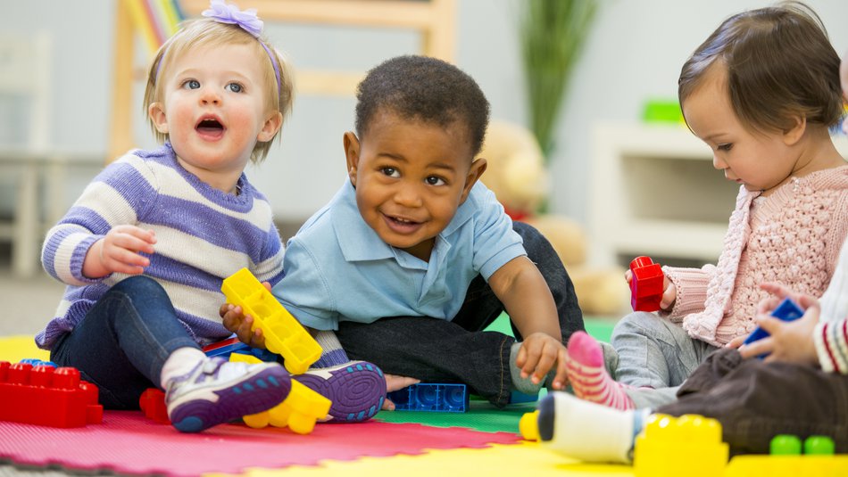 three babies sitting on a colourful mat playing with toy blocks.jpg