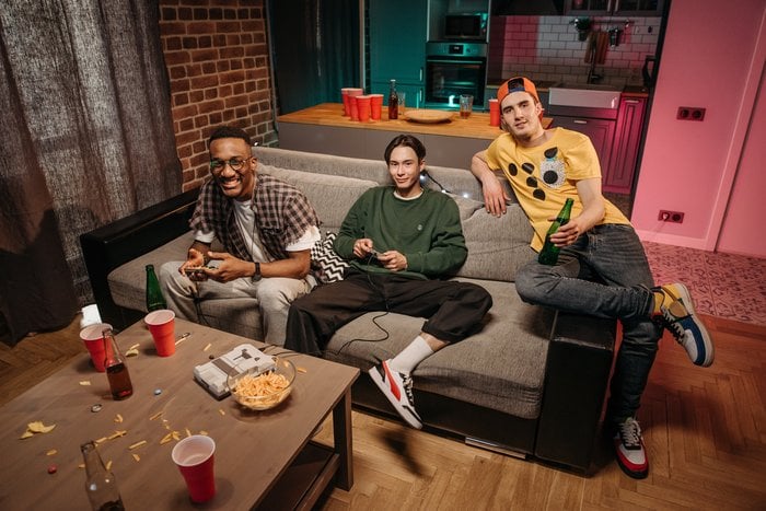 three young men sitting on couch playing video games