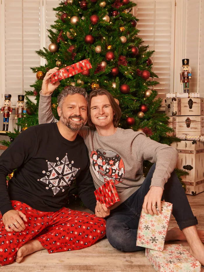 two men wearing AFC Chrsitmas Jumpers holding presents sitting in front of a christmas tree.jpg