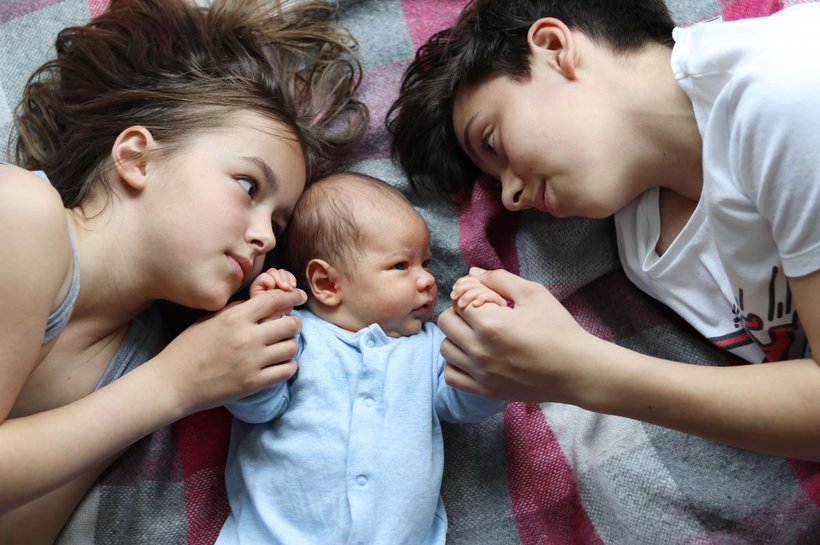 two siblings lying on a rug looking at their baby brother or sister