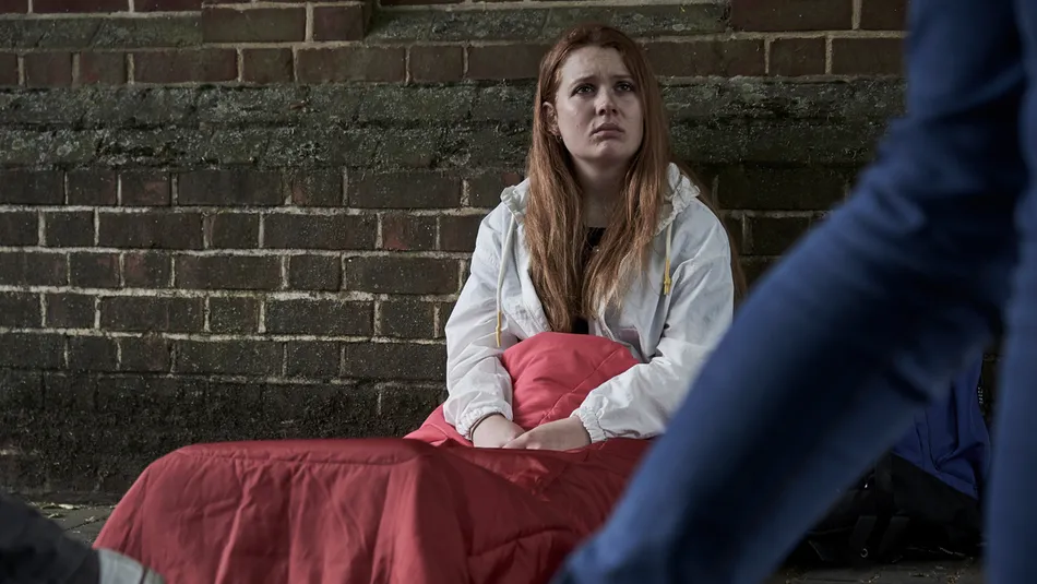 youg homeless girl sitting in sleeping back on street floor as people walk past.jpg