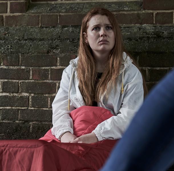 youg homeless girl sitting in sleeping back on street floor as people walk past.jpg