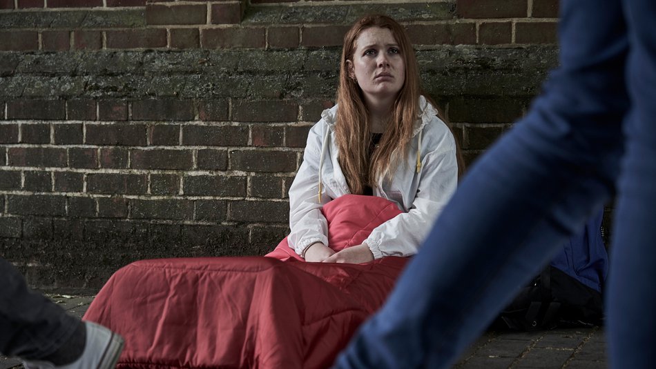 youg homeless girl sitting in sleeping back on street floor as people walk past.jpg