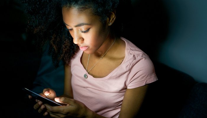 young girl sitting on bed using smartphone at night